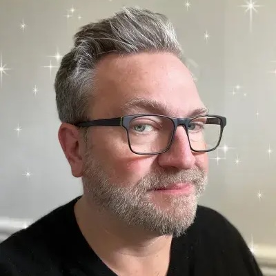 Headshot of Dan Saffer, middle aged man, shock of silver hair, glasses with dark rims, and stubble, wearing a black tshirt.